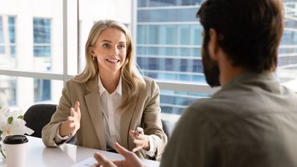 Two people discussing at a bright office table, with one woman gesturing and smiling.
