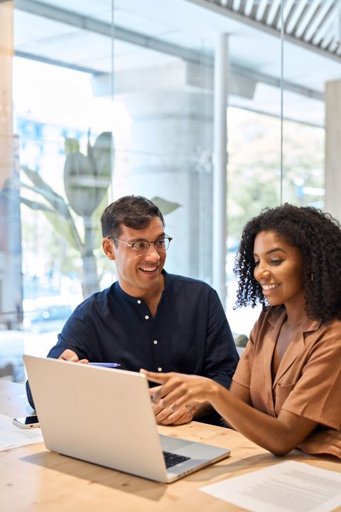Two coworkers smiling and talking at a laptop in a bright office