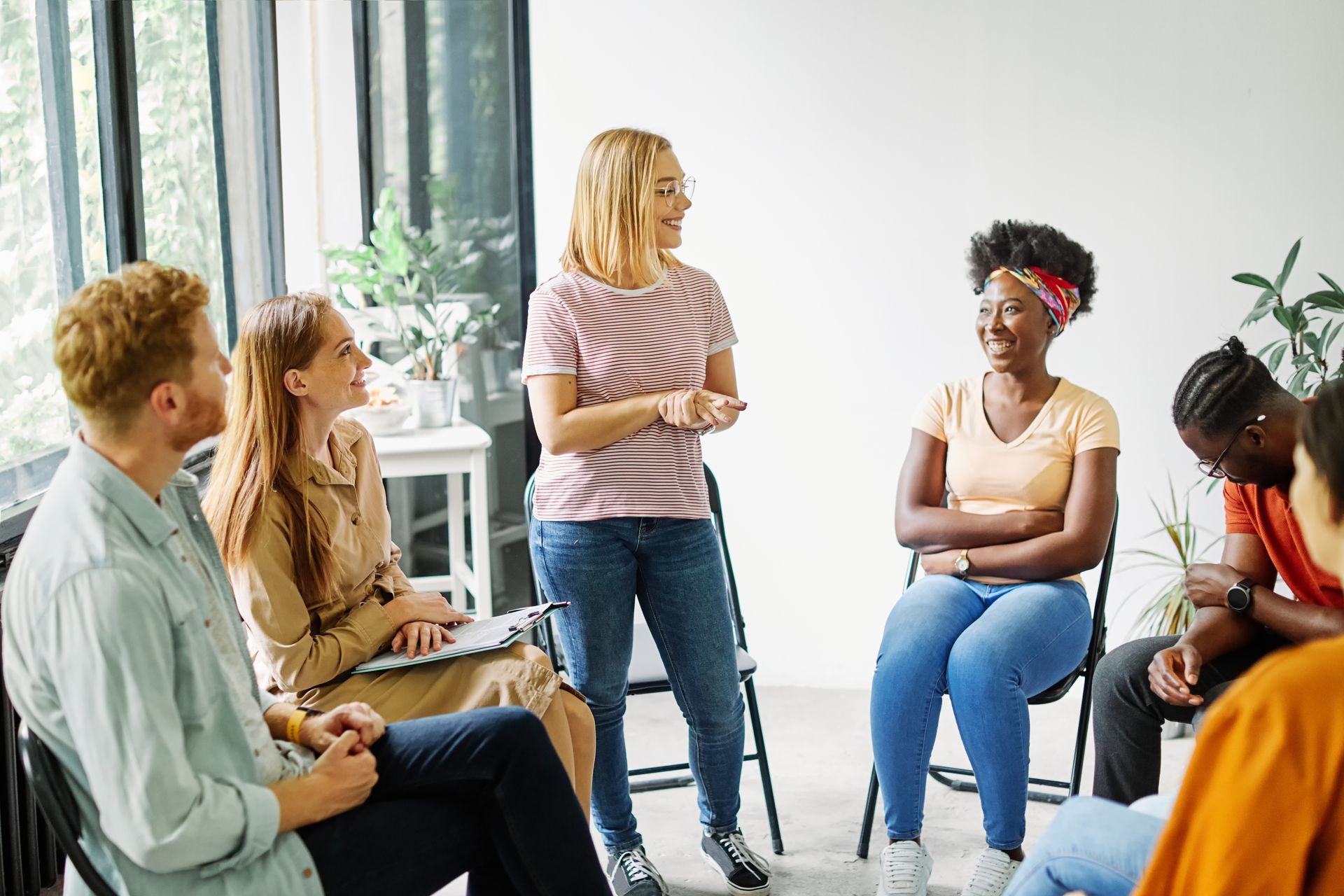 Small group in a bright room sitting in a circle, one woman speaking during a discussion.