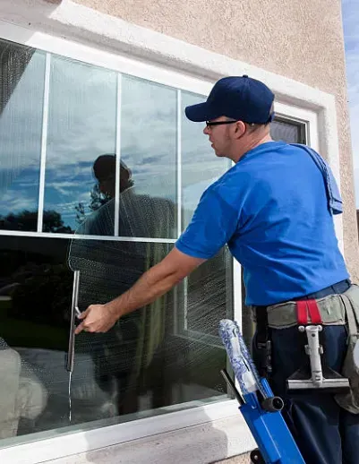 Window cleaner using a squeegee on an exterior glass door, wearing a blue uniform and cap.