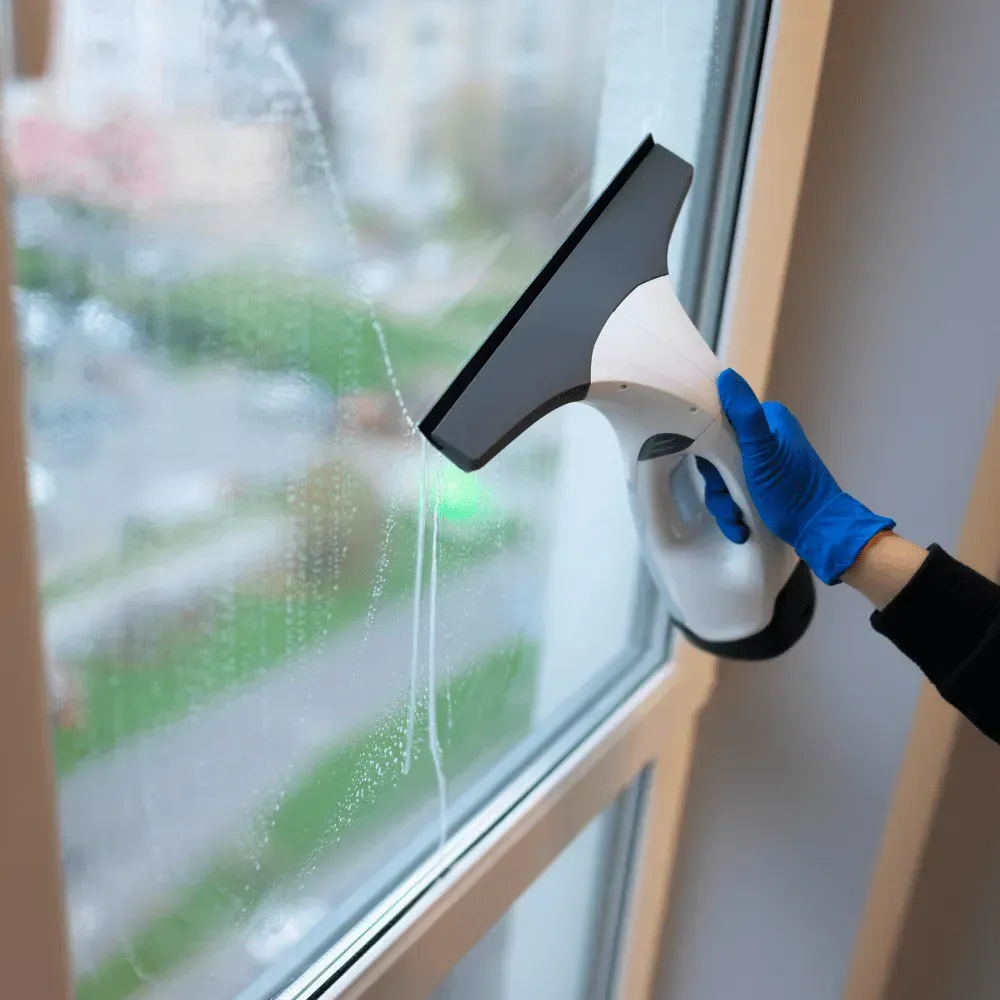 Person in blue gloves using a squeegee to clean a window indoors