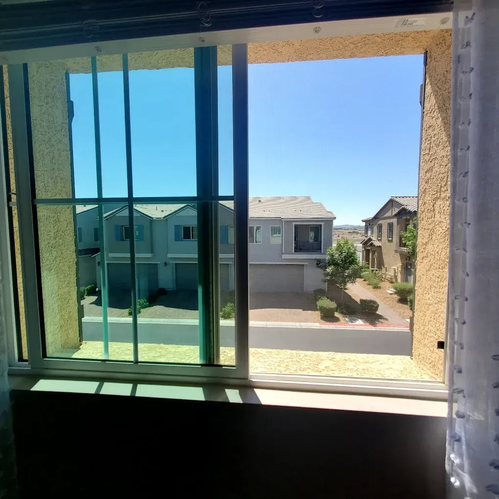 View through a window of a sunny suburban neighborhood with houses and a driveway.