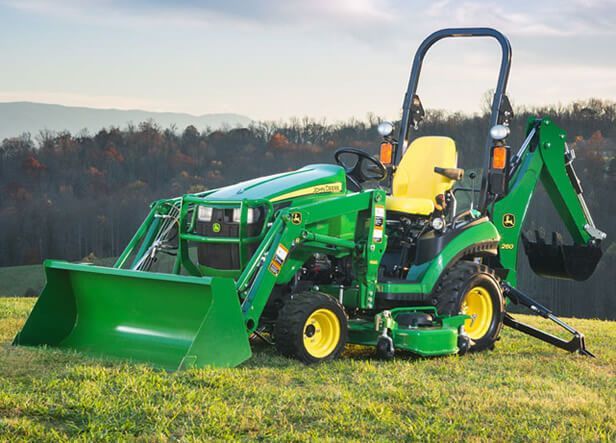 John Deere compact tractor with front bucket and backhoe in a field. Green and yellow.