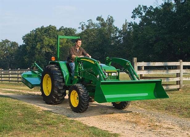 Man driving green John Deere tractor with front loader on dirt road.