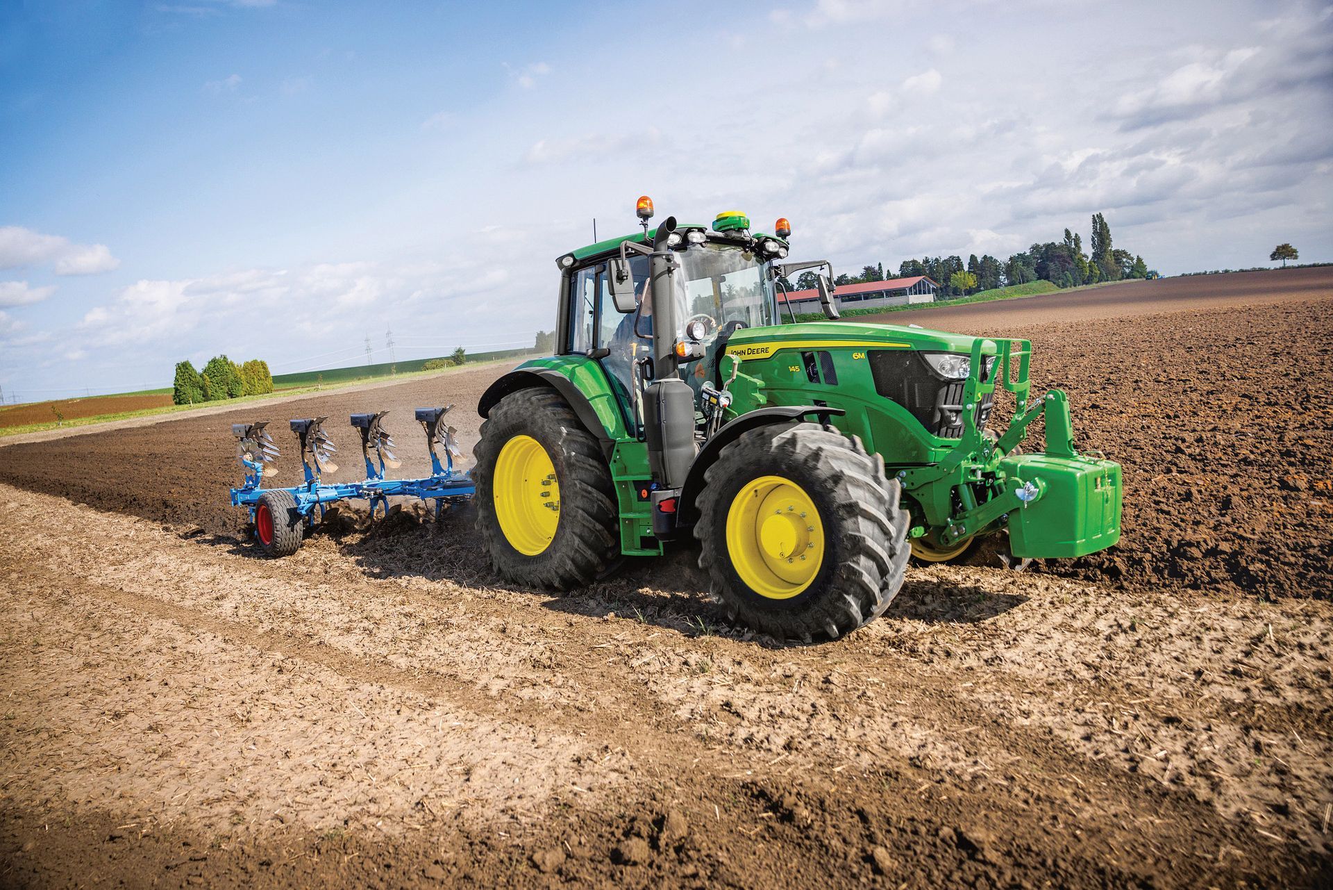 Green John Deere tractor plowing a brown field on a sunny day.