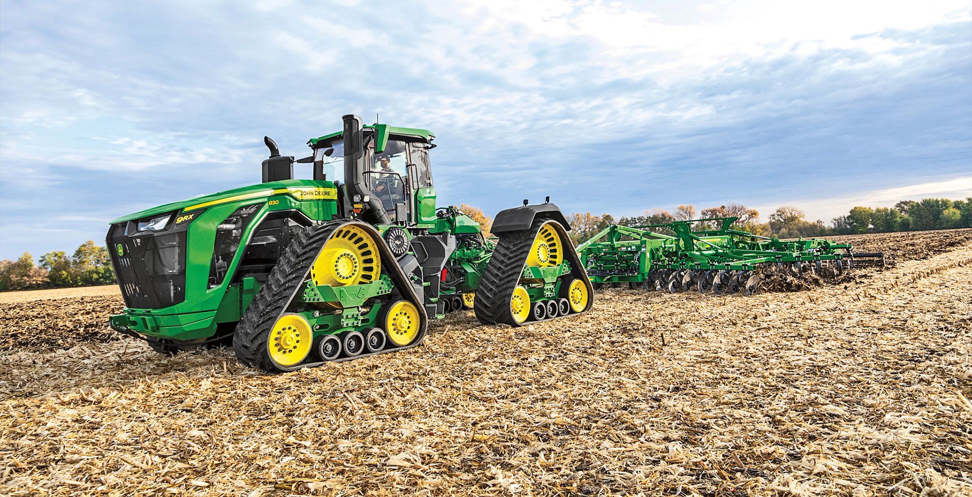 Green and yellow John Deere tractor with tracks plowing a field.