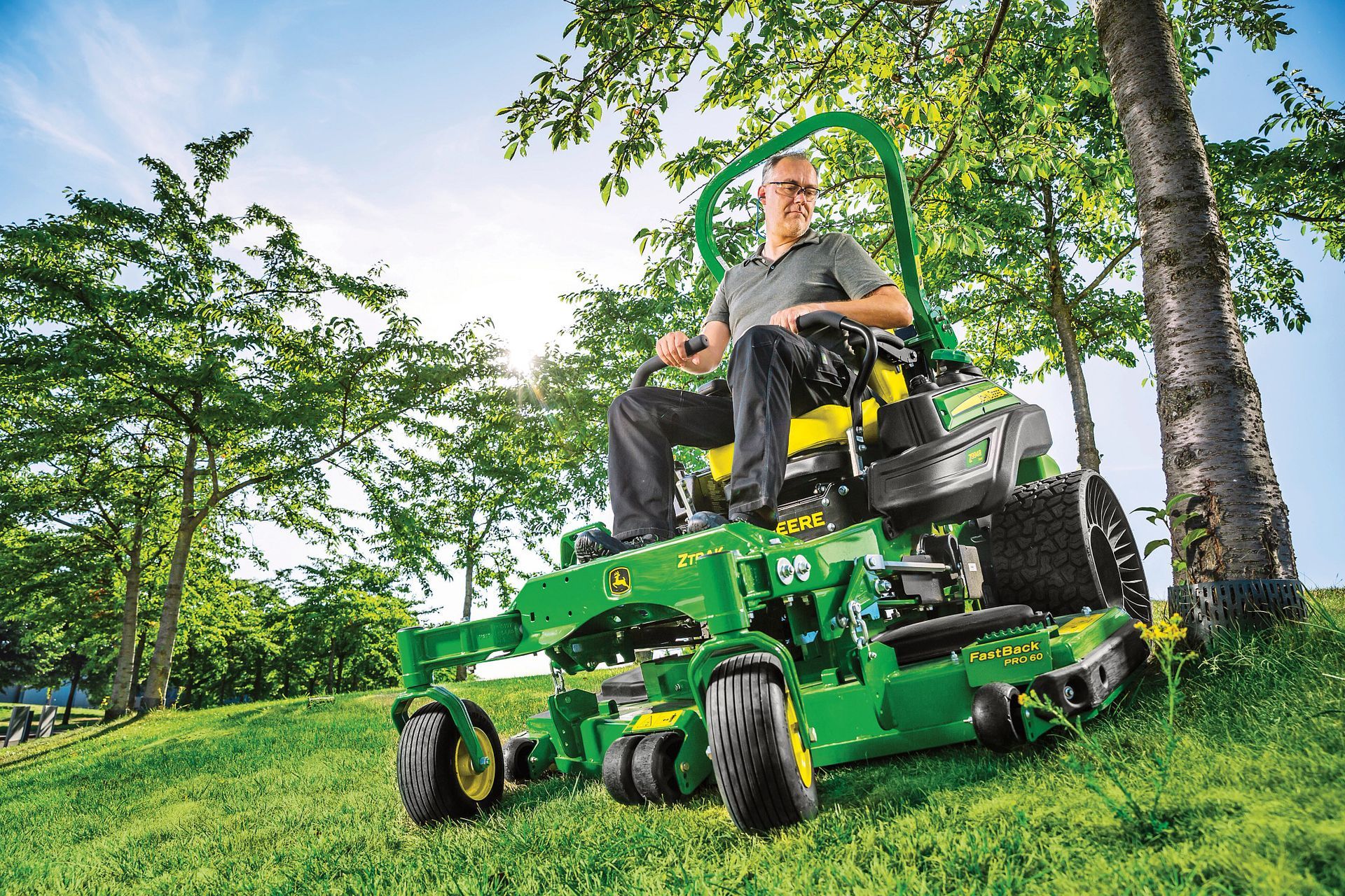 Man on a green John Deere zero-turn mower mowing a grassy hillside.