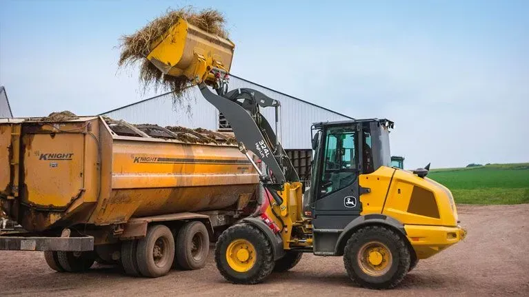 A compact wheel loader is loading hay into a dump truck.