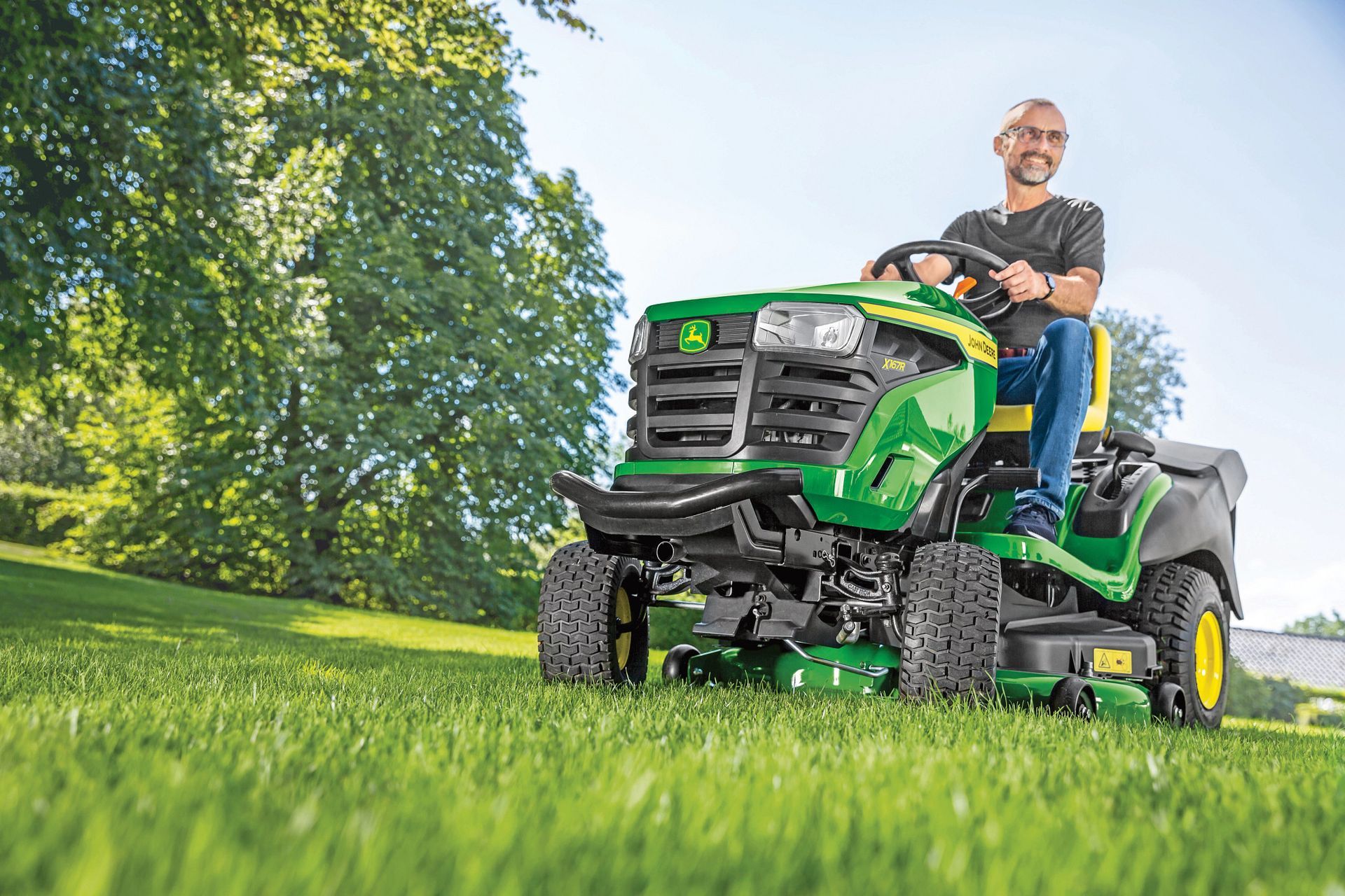 Man on a green John Deere riding lawnmower cutting grass on a sunny day.