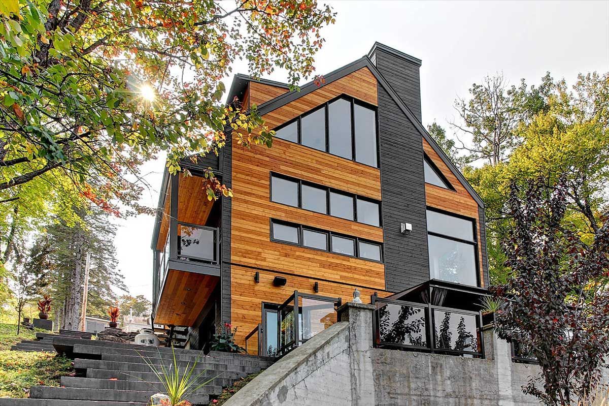 Maison moderne revêtue de bois avec des touches de noir, de grandes fenêtres et une base en béton, vue d'en bas.
