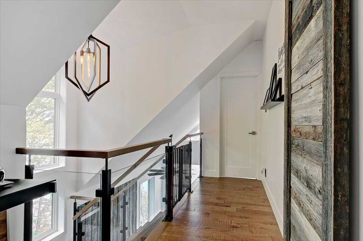 Couloir avec parquet, rampe en métal noir et luminaire géométrique.