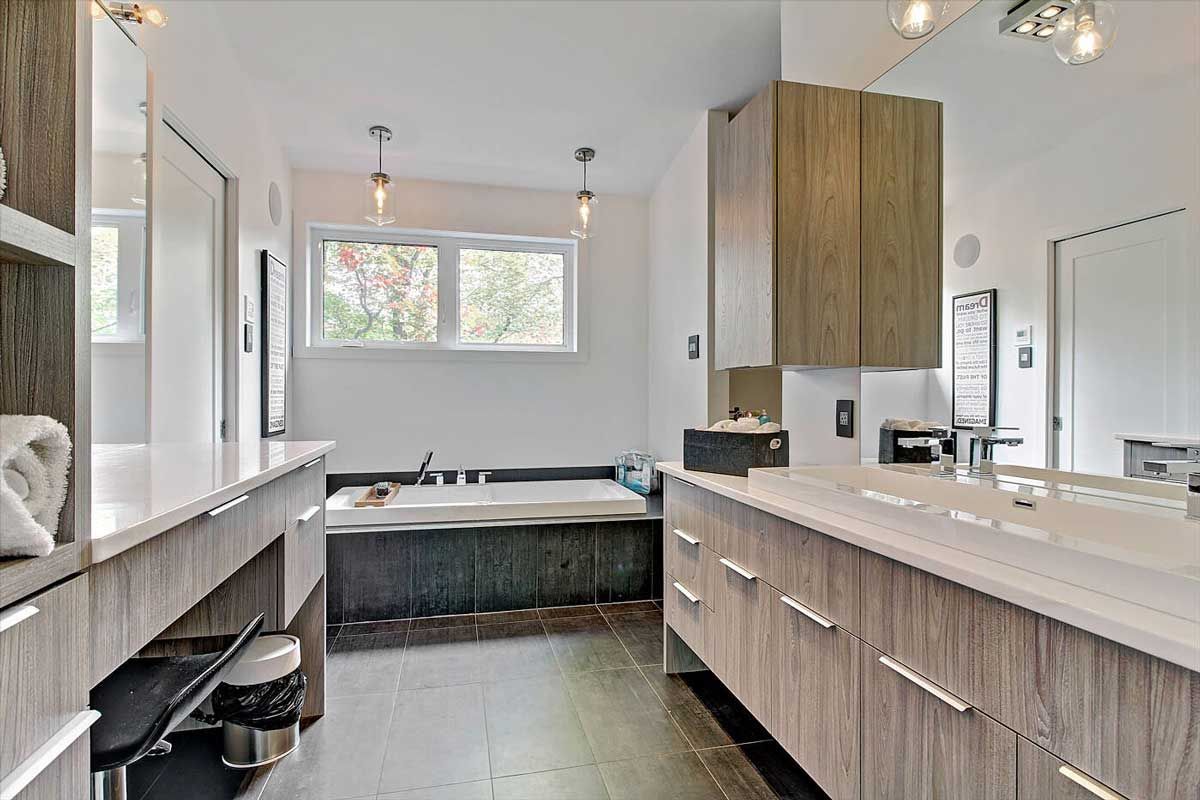 Salle de bains moderne avec double vasque, baignoire encastrée et fenêtre. Meubles en bois et plans de travail blancs.
