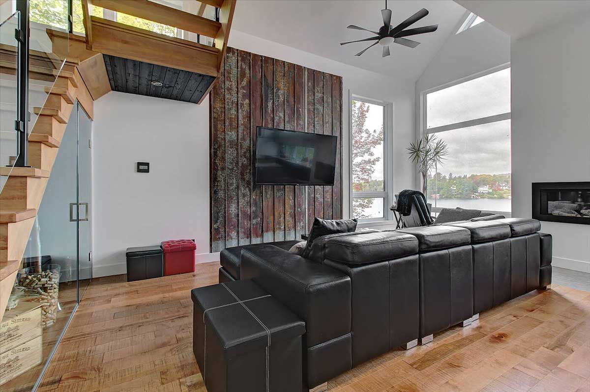 Salon avec canapé d'angle noir, parquet et télévision fixée au mur en bois.