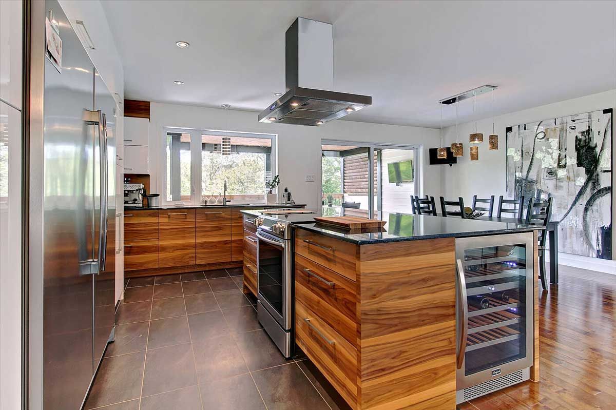 Cuisine moderne avec armoires en bois, îlot central, électroménagers en acier inoxydable et coin repas.