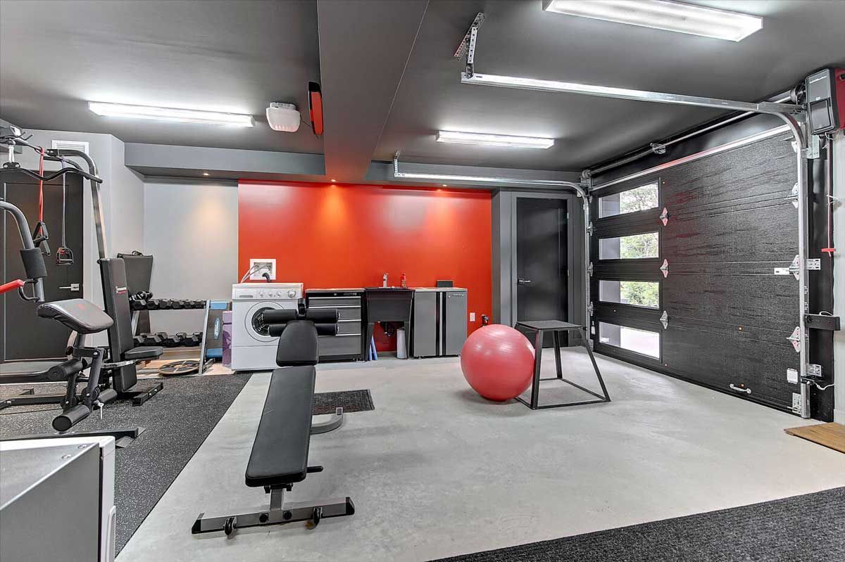 Salle de sport à domicile aménagée dans un garage transformé, avec haltères, banc et mur d'accent rouge.