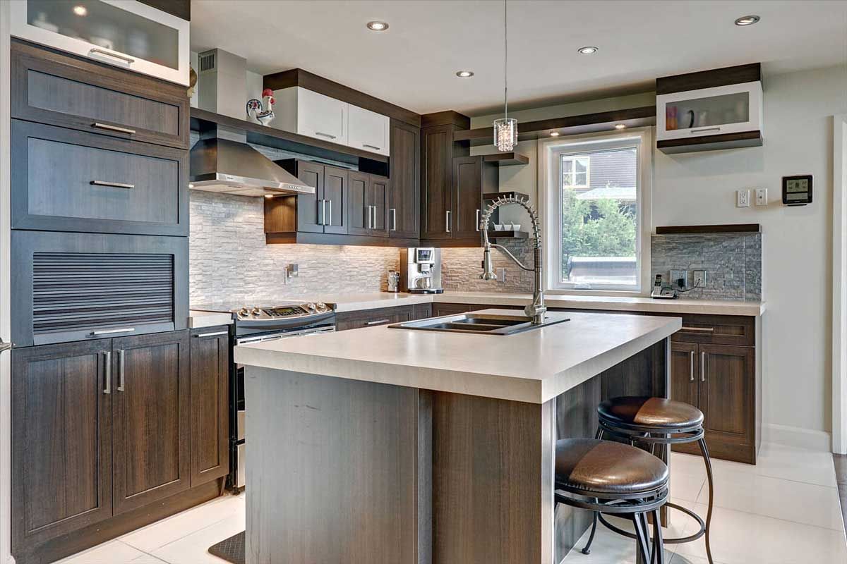 Cuisine moderne avec armoires en bois foncé, îlot central clair et appareils électroménagers en acier inoxydable.