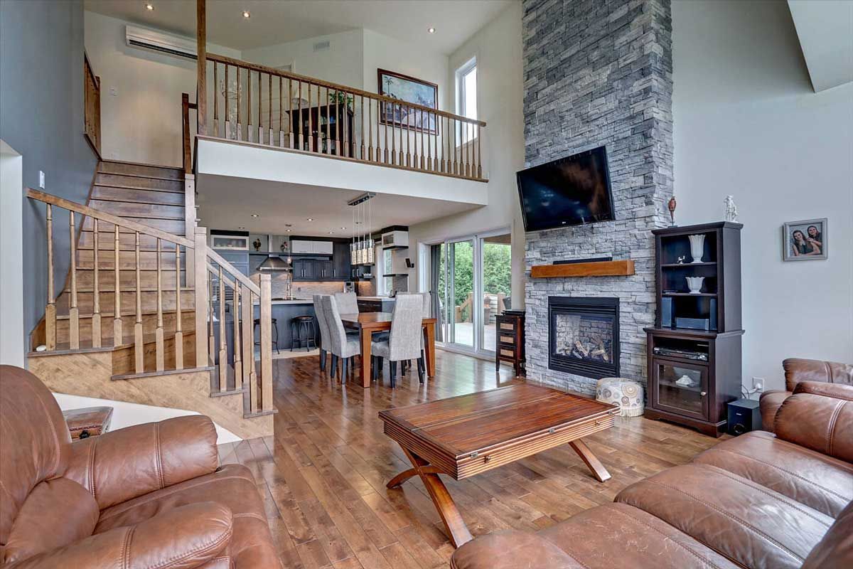 Salon avec mezzanine, cheminée en pierre, parquet et meubles en cuir.