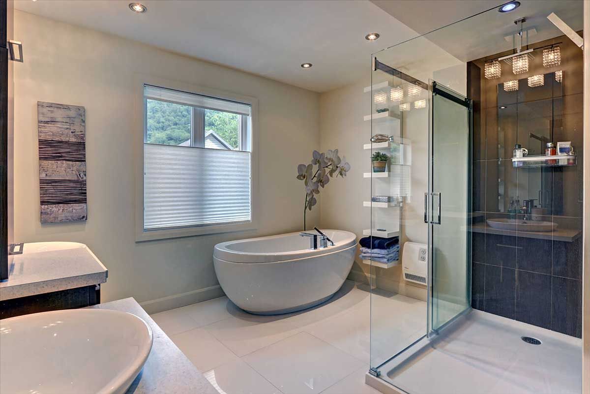 Salle de bains moderne avec baignoire, douche et lavabo blancs. Couleurs neutres, lumière naturelle et éléments décoratifs.