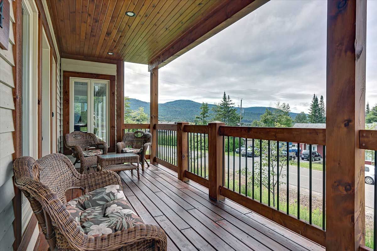 Véranda en bois avec mobilier en osier donnant sur une vue sur la montagne.
