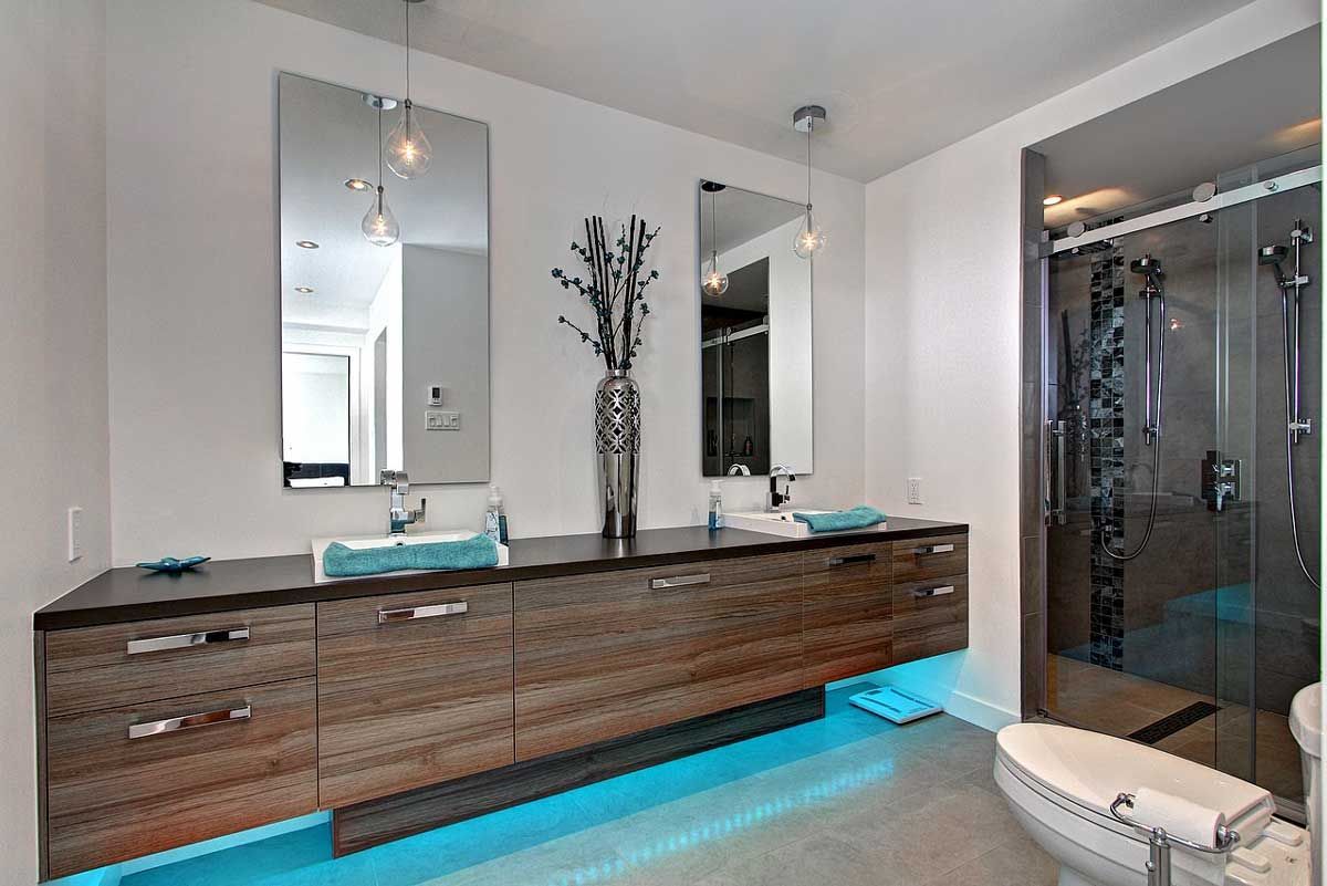 Salle de bains moderne avec double vasque, grands miroirs, douche et éclairage bleu sous les meubles.