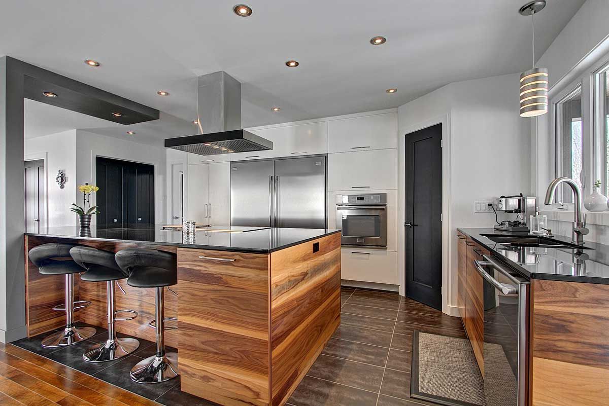 Cuisine moderne avec des touches de bois et de noir, des appareils électroménagers en acier inoxydable et un îlot avec tabourets de bar.