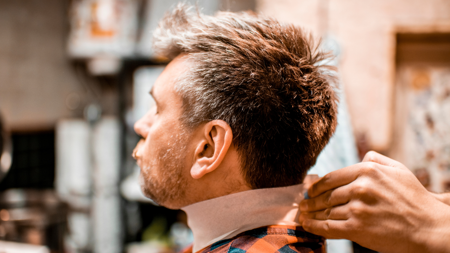 A person’s neck is being wrapped in a paper barber collar by a hand in a dimly lit, professional salon setting.