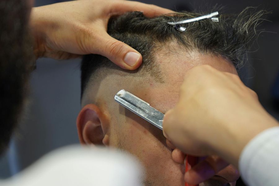 Barber shaving a client’s hairline with clippers and a straight razor