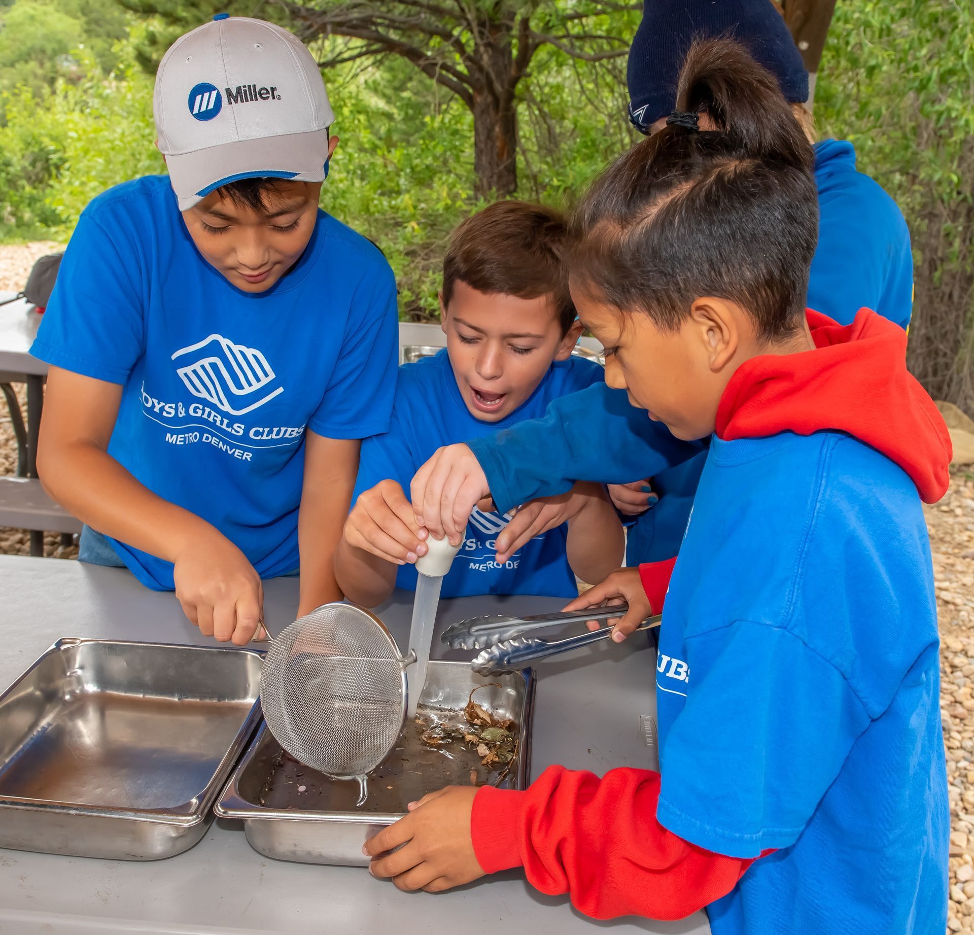 A boy wearing a miller hat is helping a girl scoop something out of a container