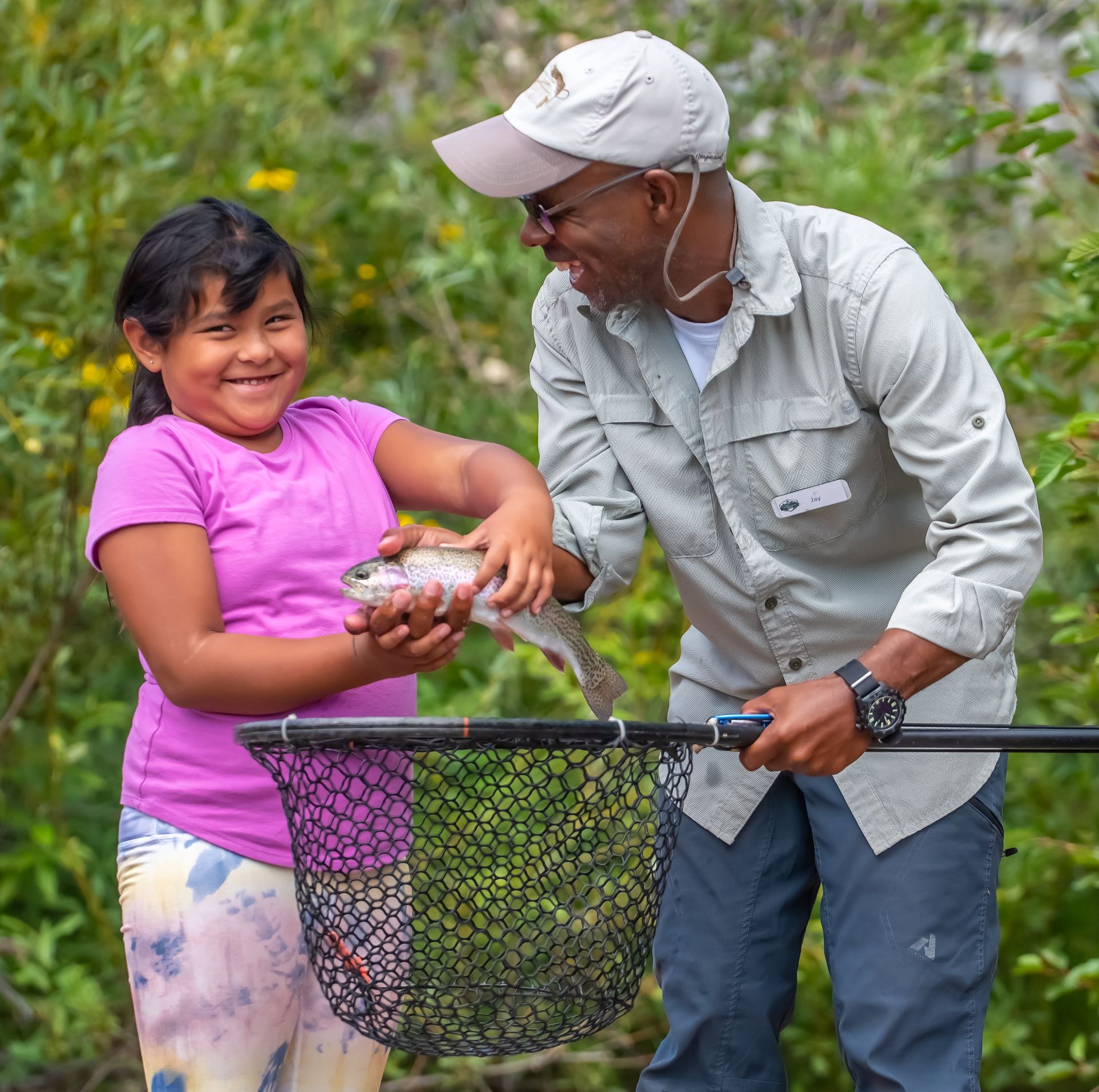 A man and a little girl are holding a fish in a net.