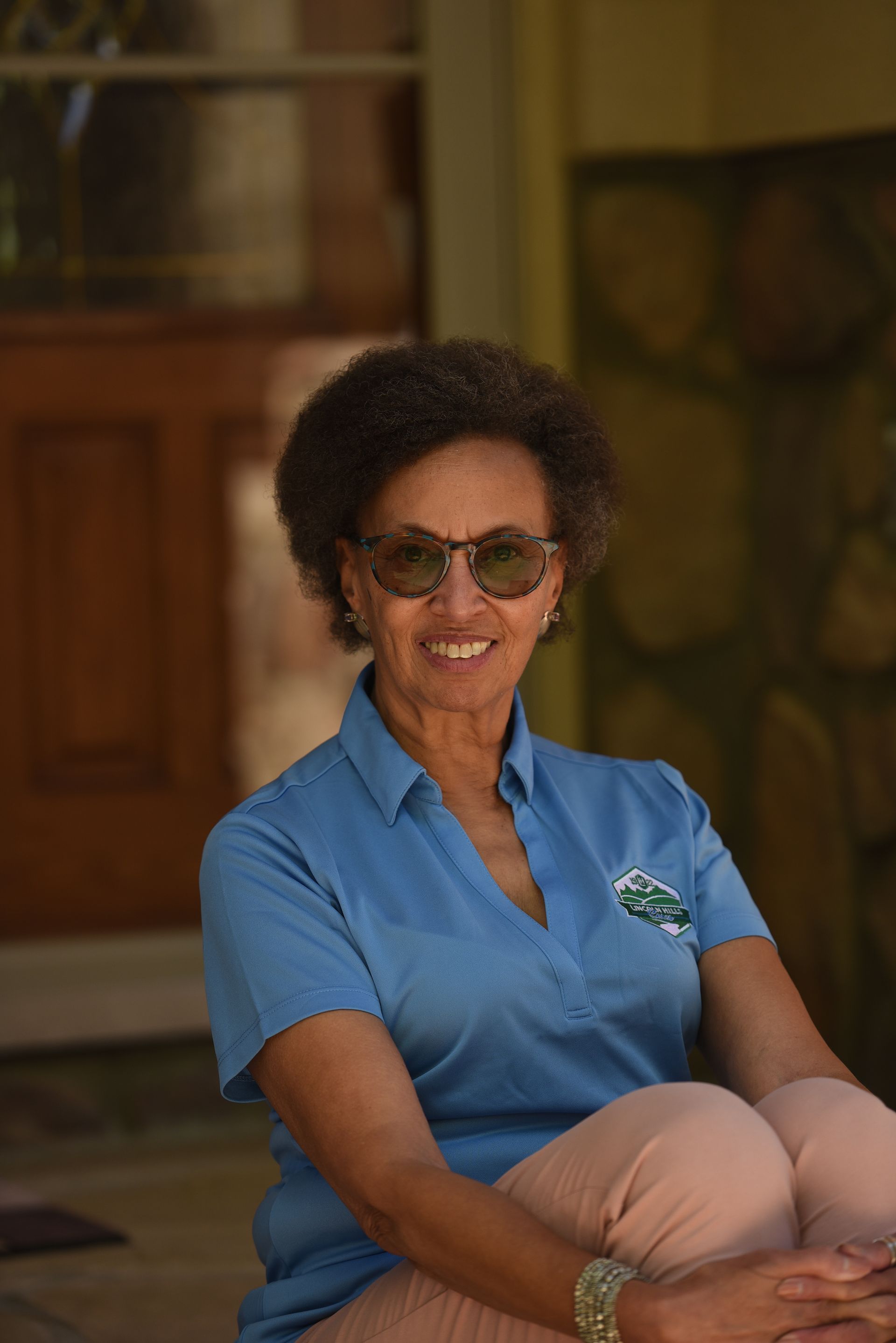 A woman wearing sunglasses and a blue shirt is sitting on the ground.
