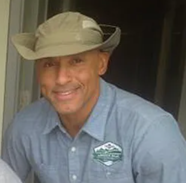 A man wearing a cowboy hat and a blue shirt is smiling.