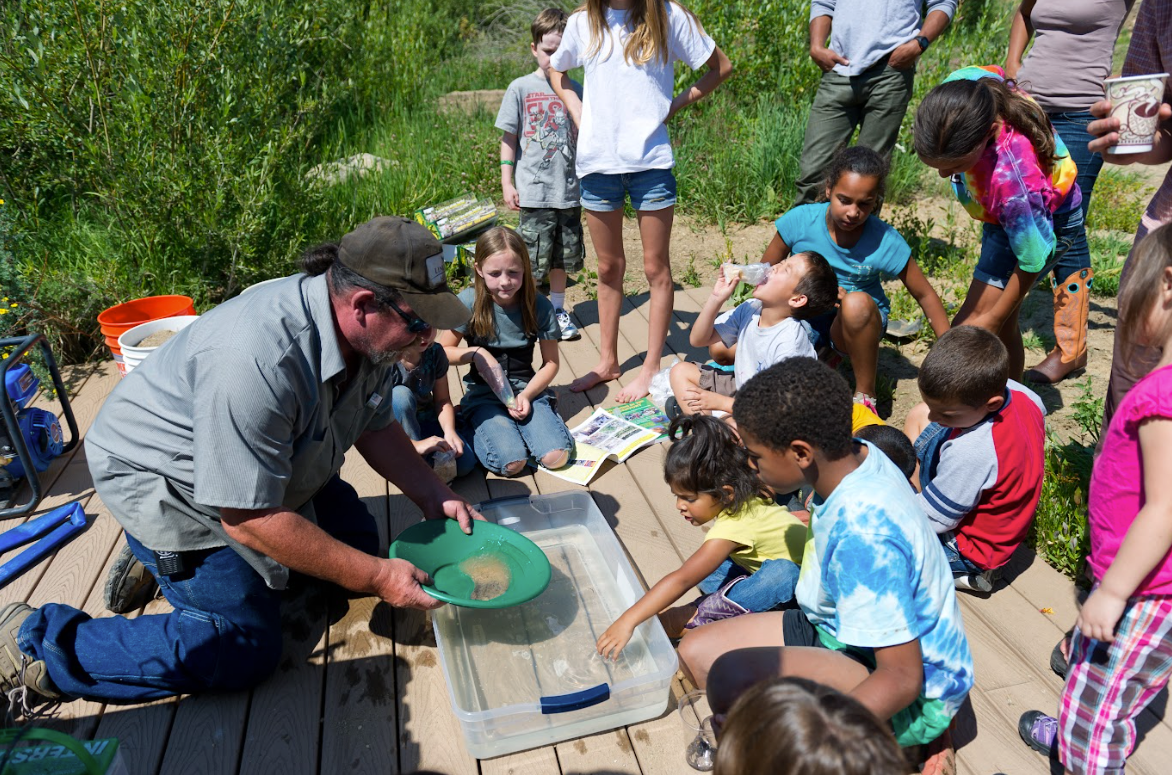 A group of children are sitting around a man on a deck.