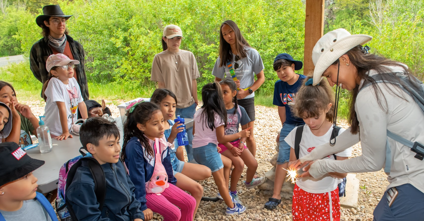 A woman in a cowboy hat is talking to a group of children.
