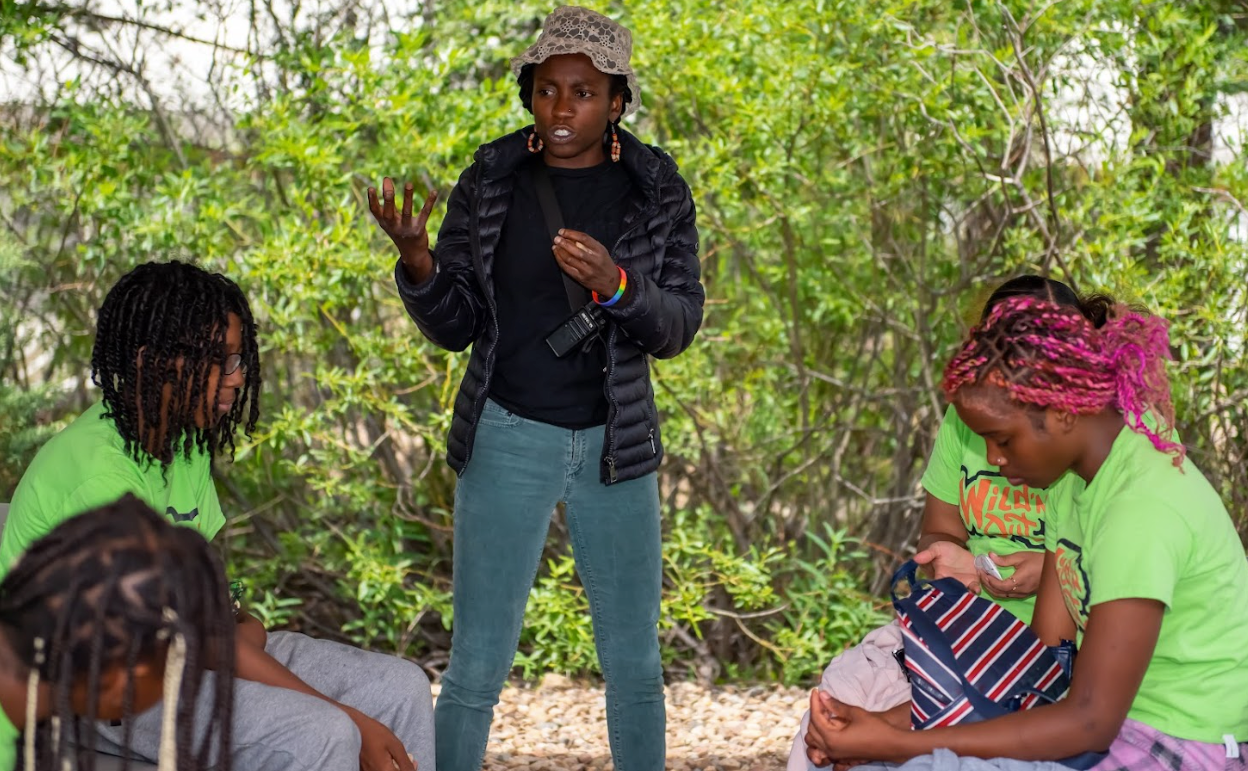 A woman is standing in front of a group of people sitting in a circle.