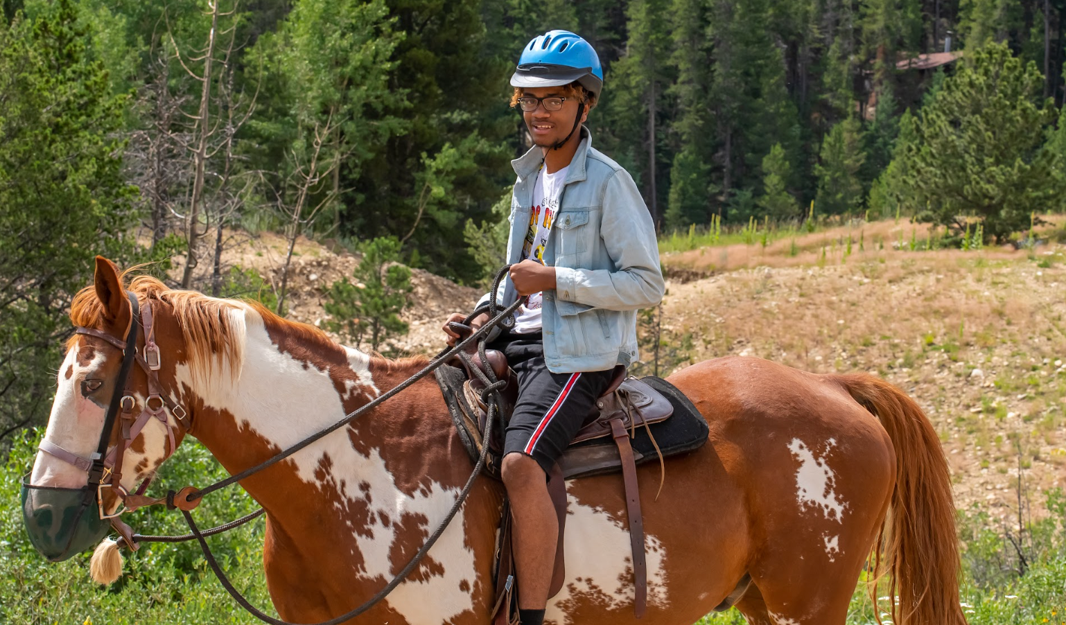 A young man is riding a brown and white horse in a field.