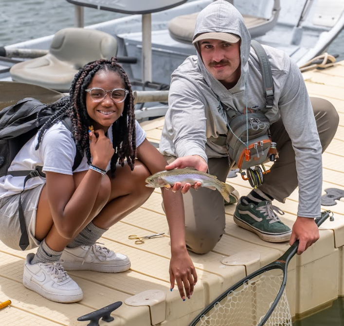 A man and a woman are kneeling on a dock holding a fish