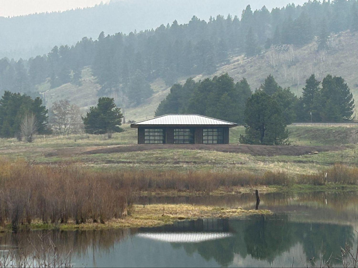 A small house in the middle of a field next to a lake