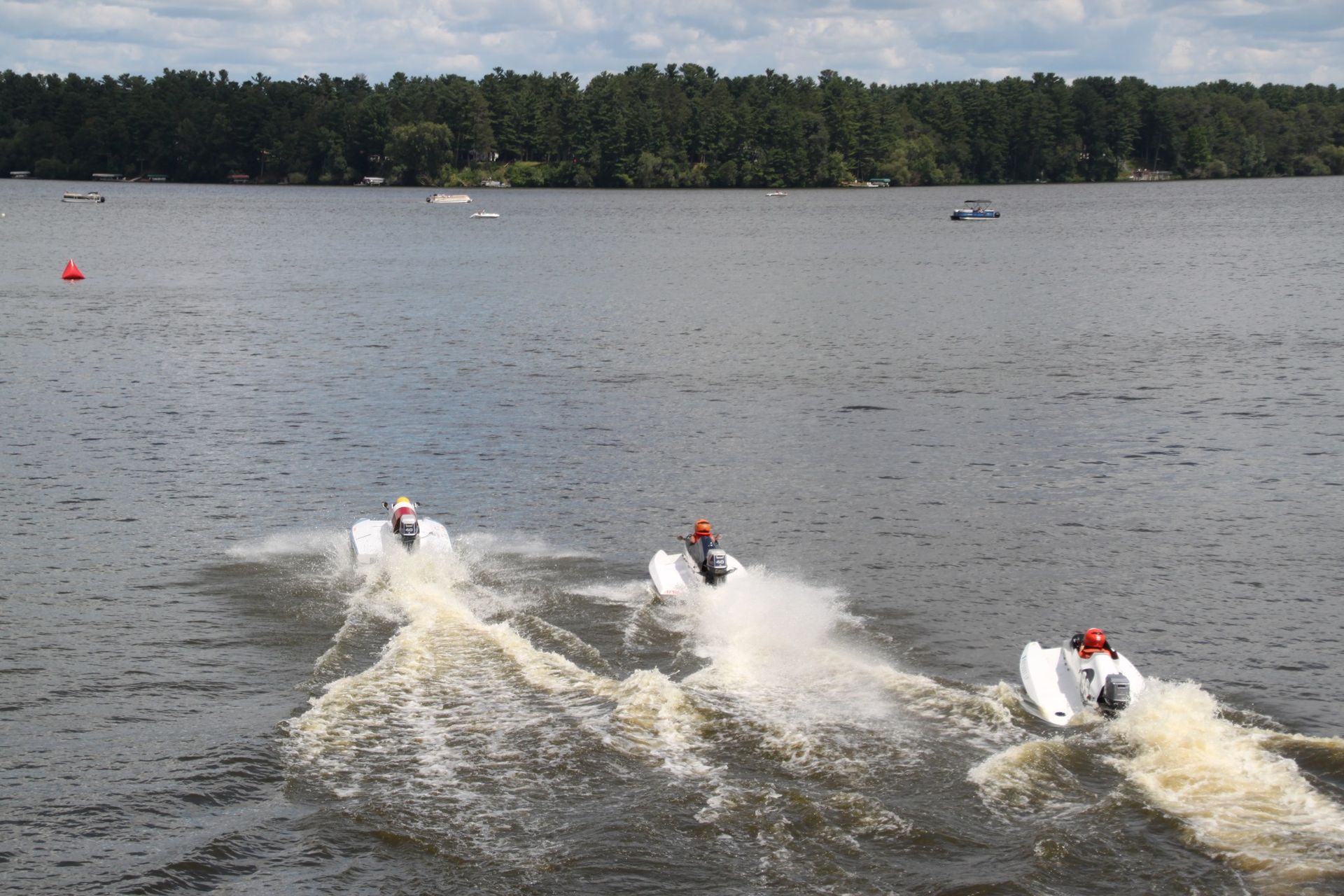 Two boats are racing on a lake with trees in the background