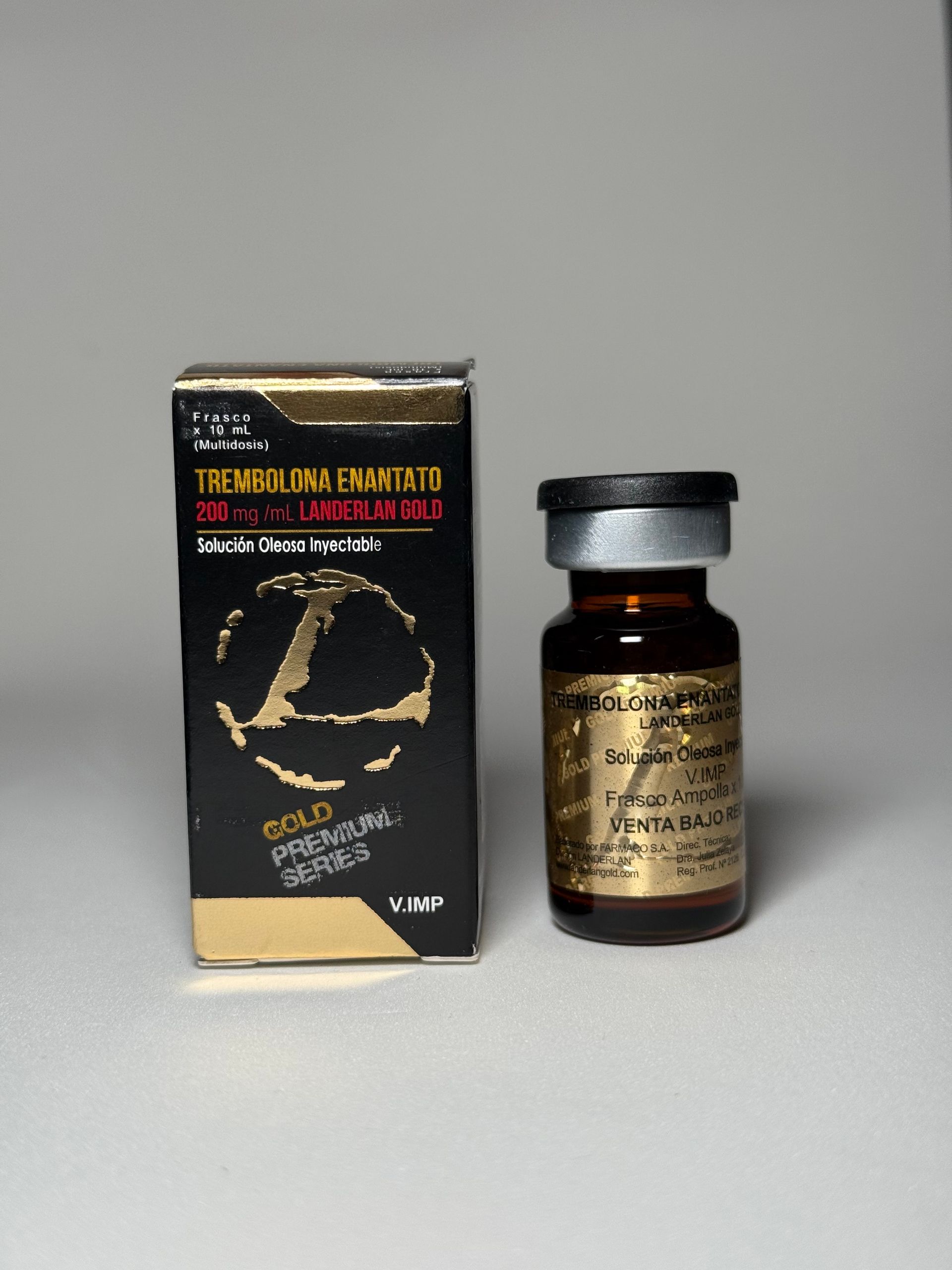 Un vial de medicamento líquido y su caja. La caja negra tiene texto y un logotipo dorados. Frasco de medicamento marrón.