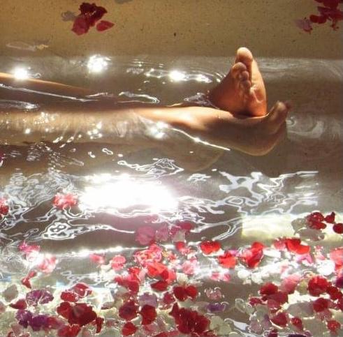 Een persoon ligt in een badkuip omringd door bloemen