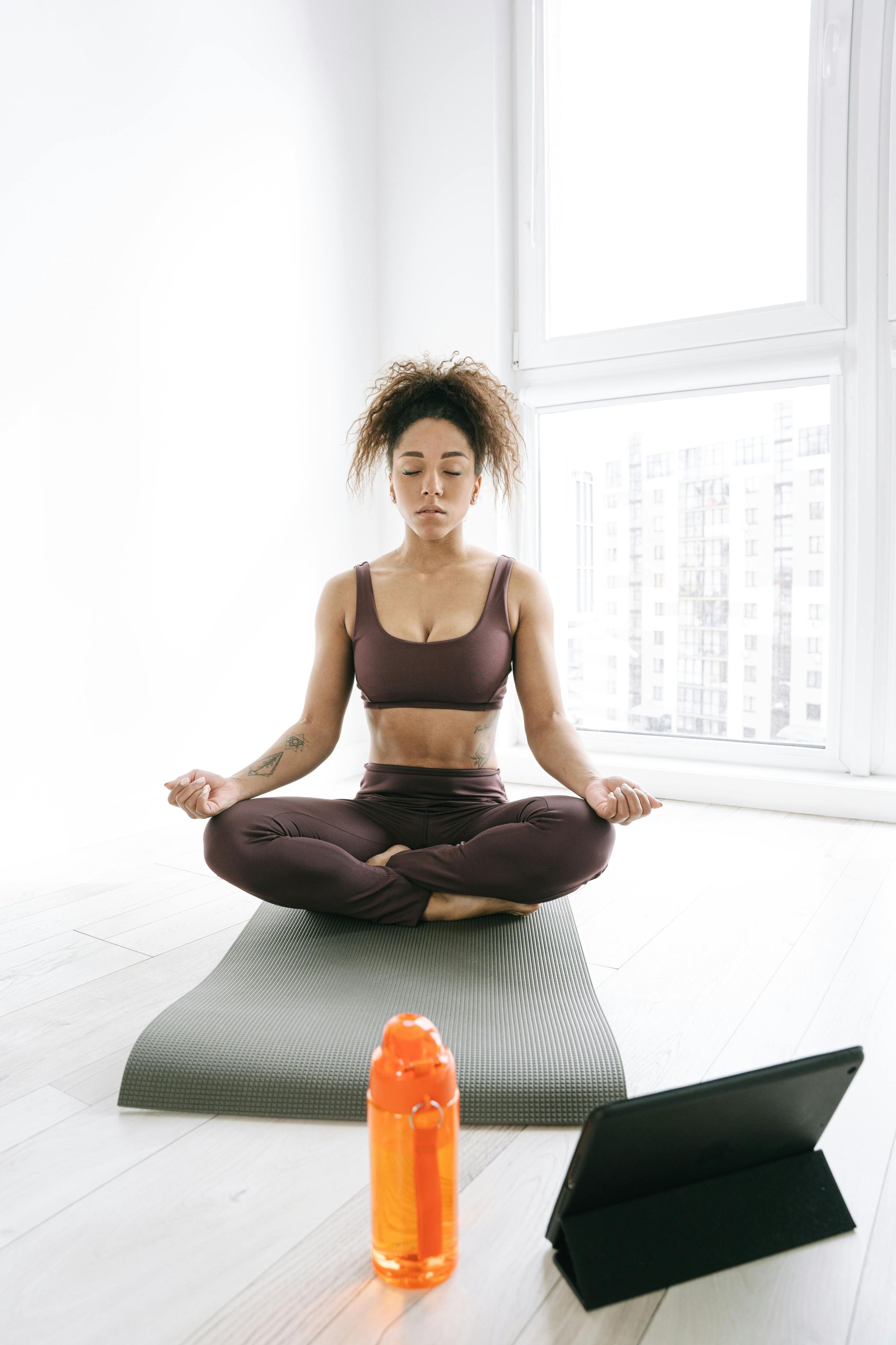 Een vrouw zit op een yogamat voor een tablet.