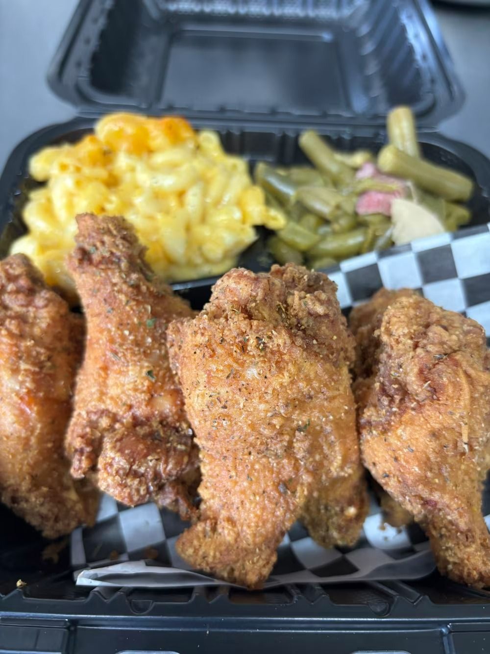 Fried chicken wings with mac and cheese and green beans in a black takeout container.