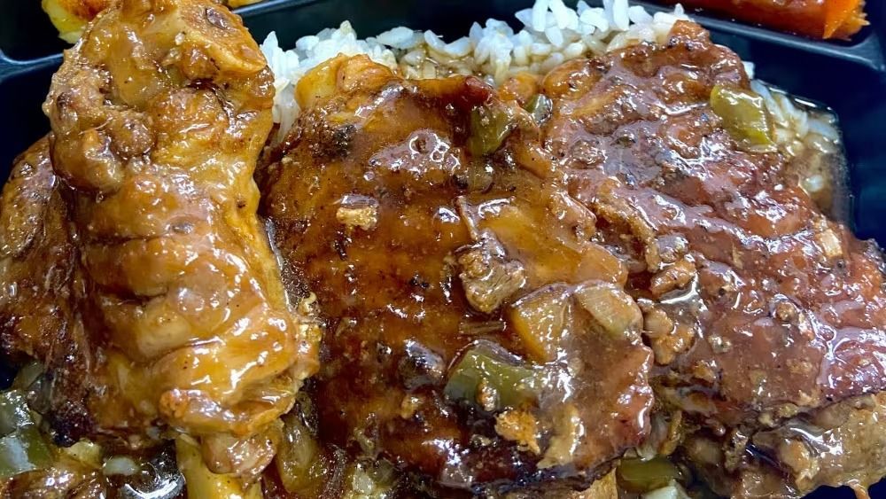 Stewed meat in brown gravy over white rice in a black food container.
