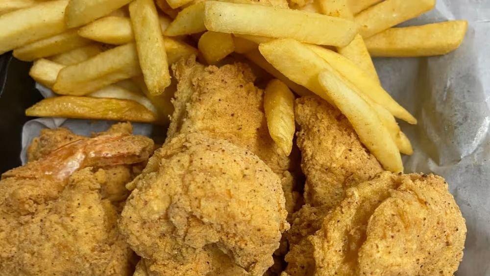 Fried fish and fries, golden brown, served in a black container.