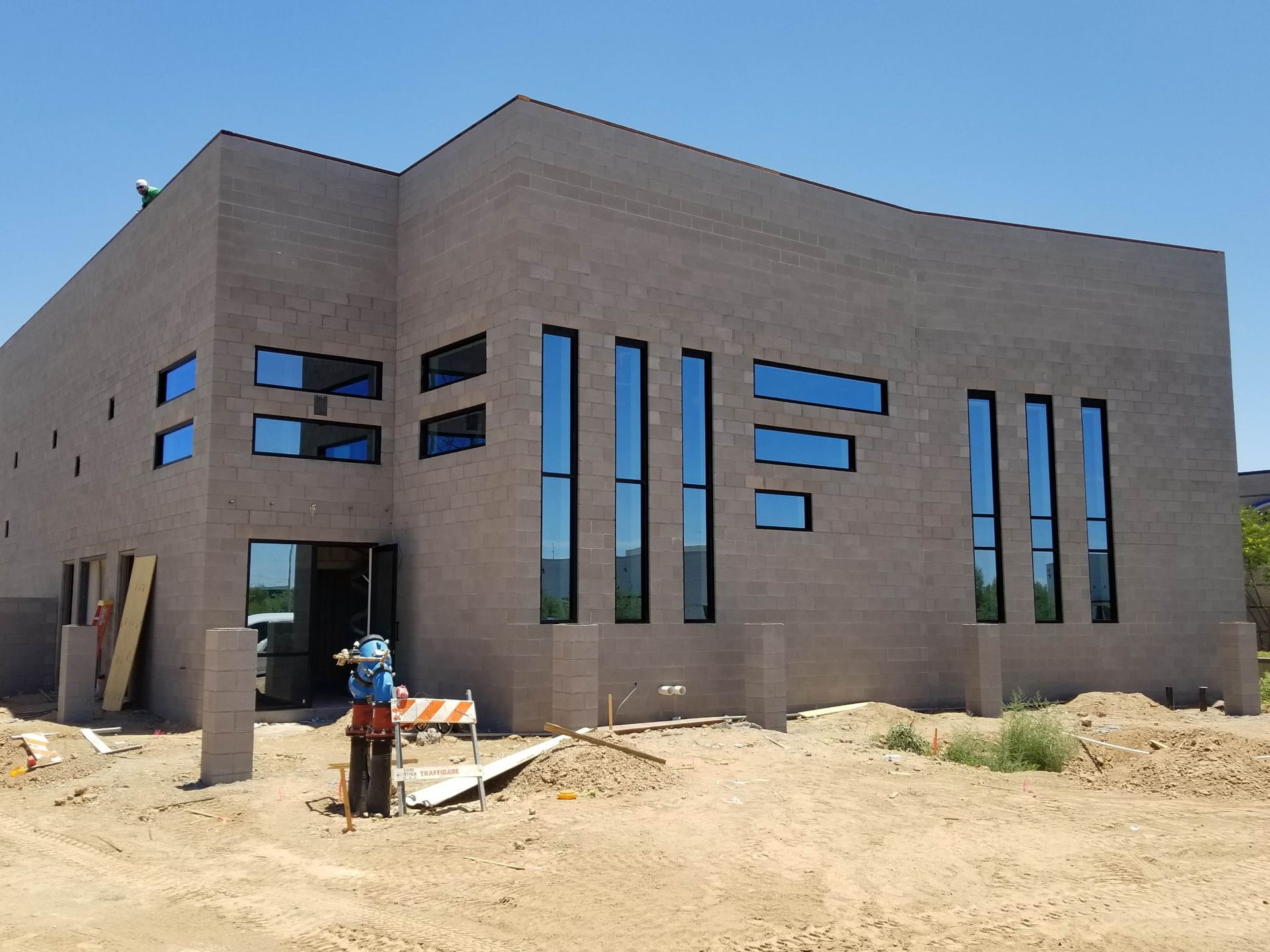 Building under construction with rectangular windows; gray brick exterior, bright blue sky.