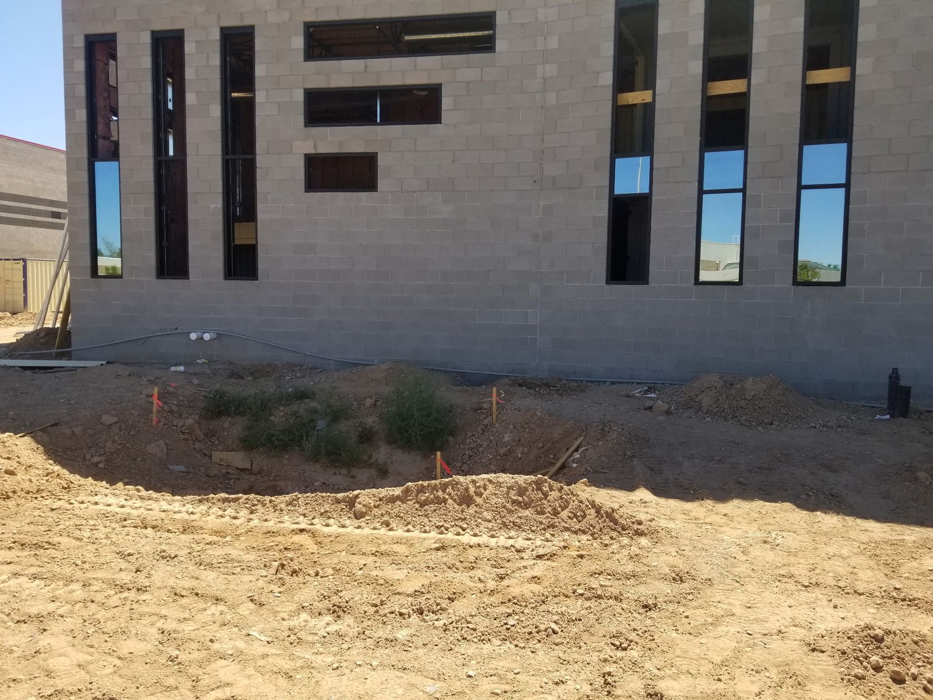 Building under construction with tall rectangular windows, set against a sandy, barren landscape.