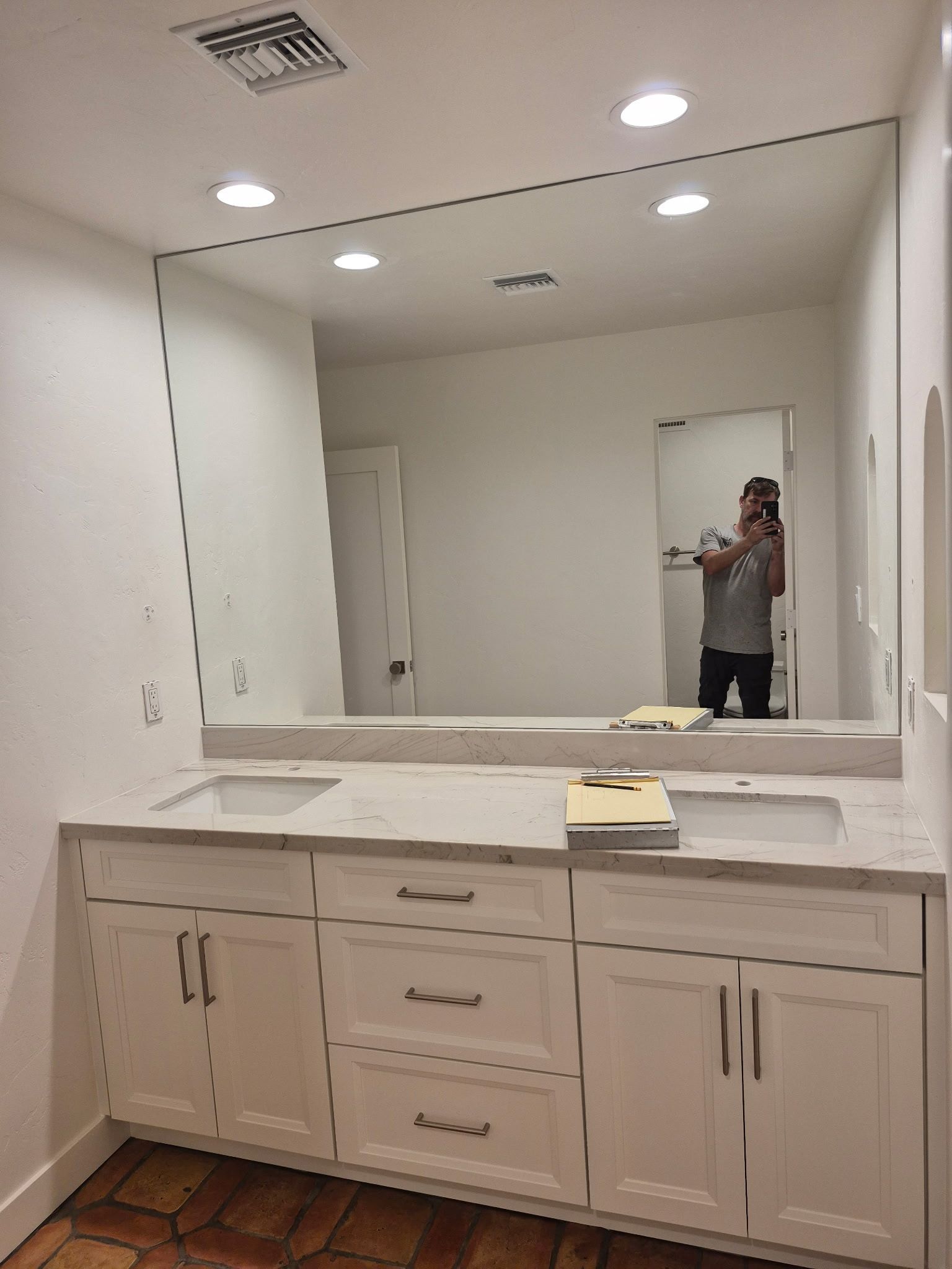 Bathroom with white cabinets, large mirror, and person taking a photo.