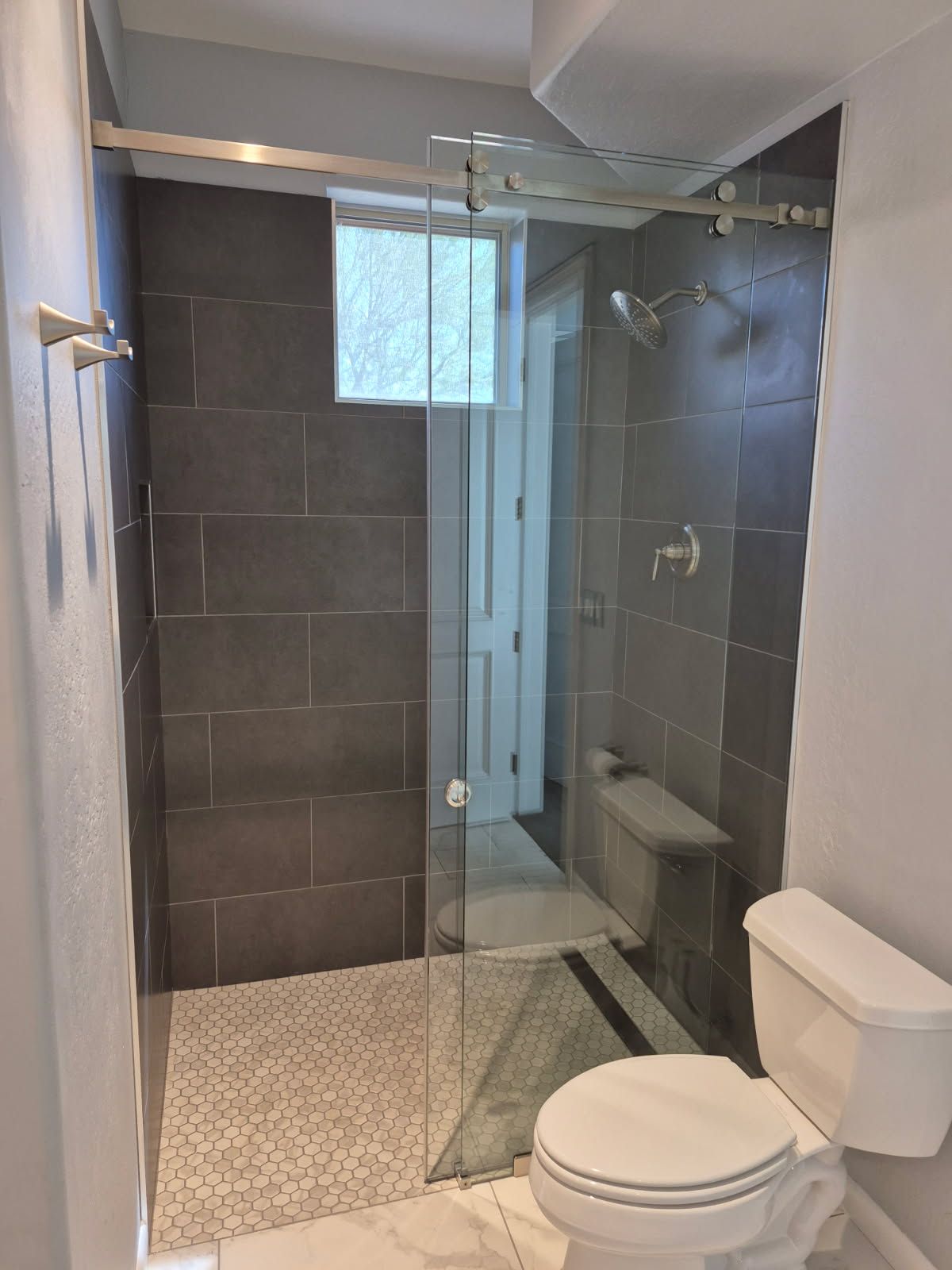 Modern bathroom with a frameless shower, toilet, and dark gray tiles.