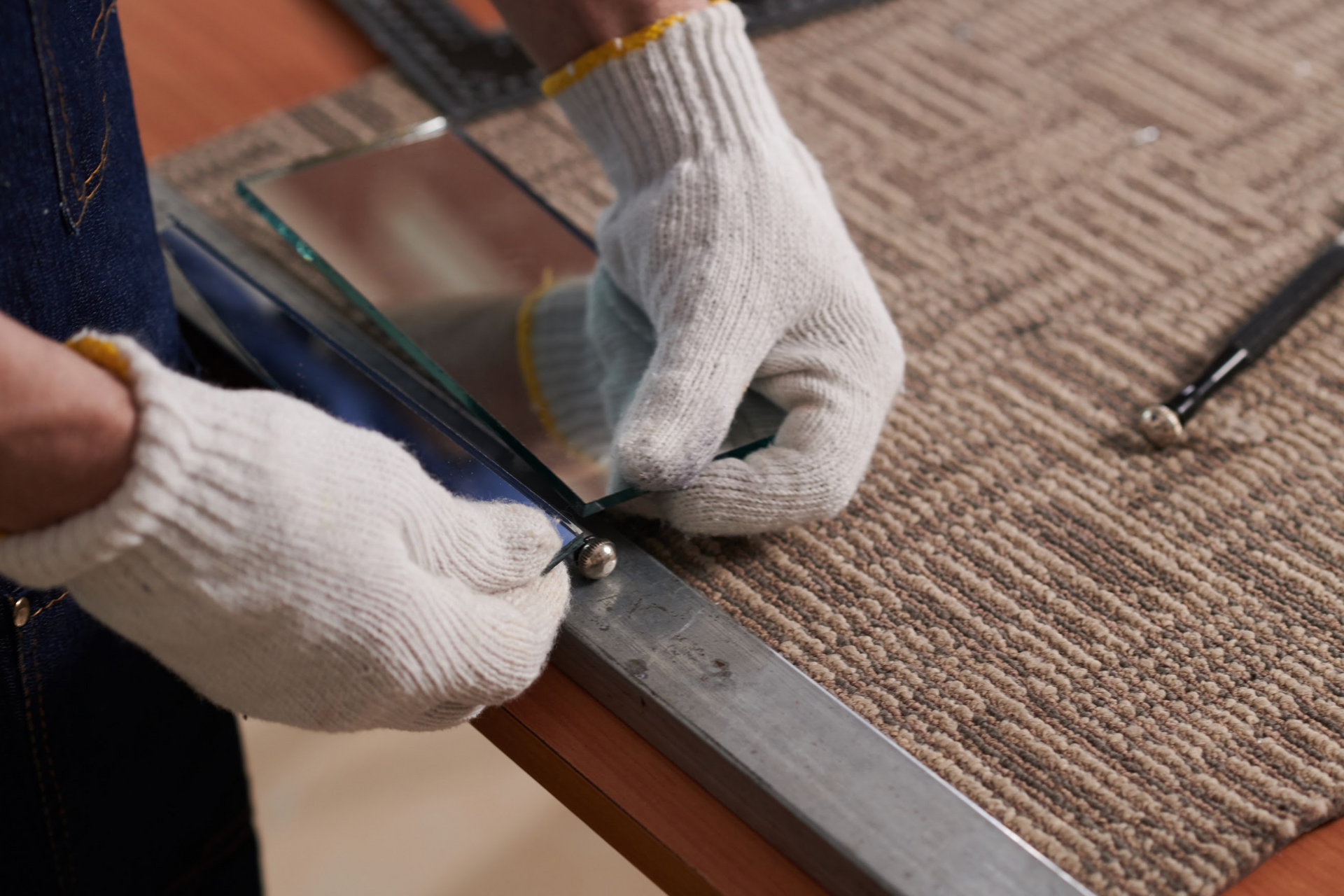Person wearing gloves scoring glass with a tool, preparing to cut it.