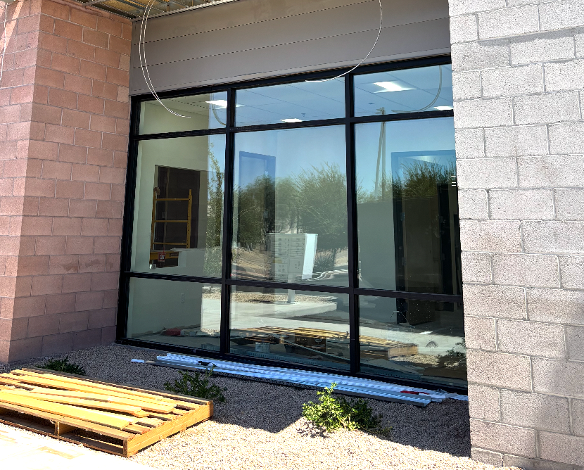 Large window on a brick building exterior, black frame, showing unfinished interior, gravel, and landscaping.